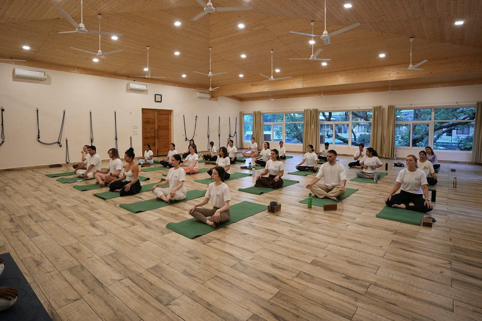 A full yoga class seated on mats in a studio hall