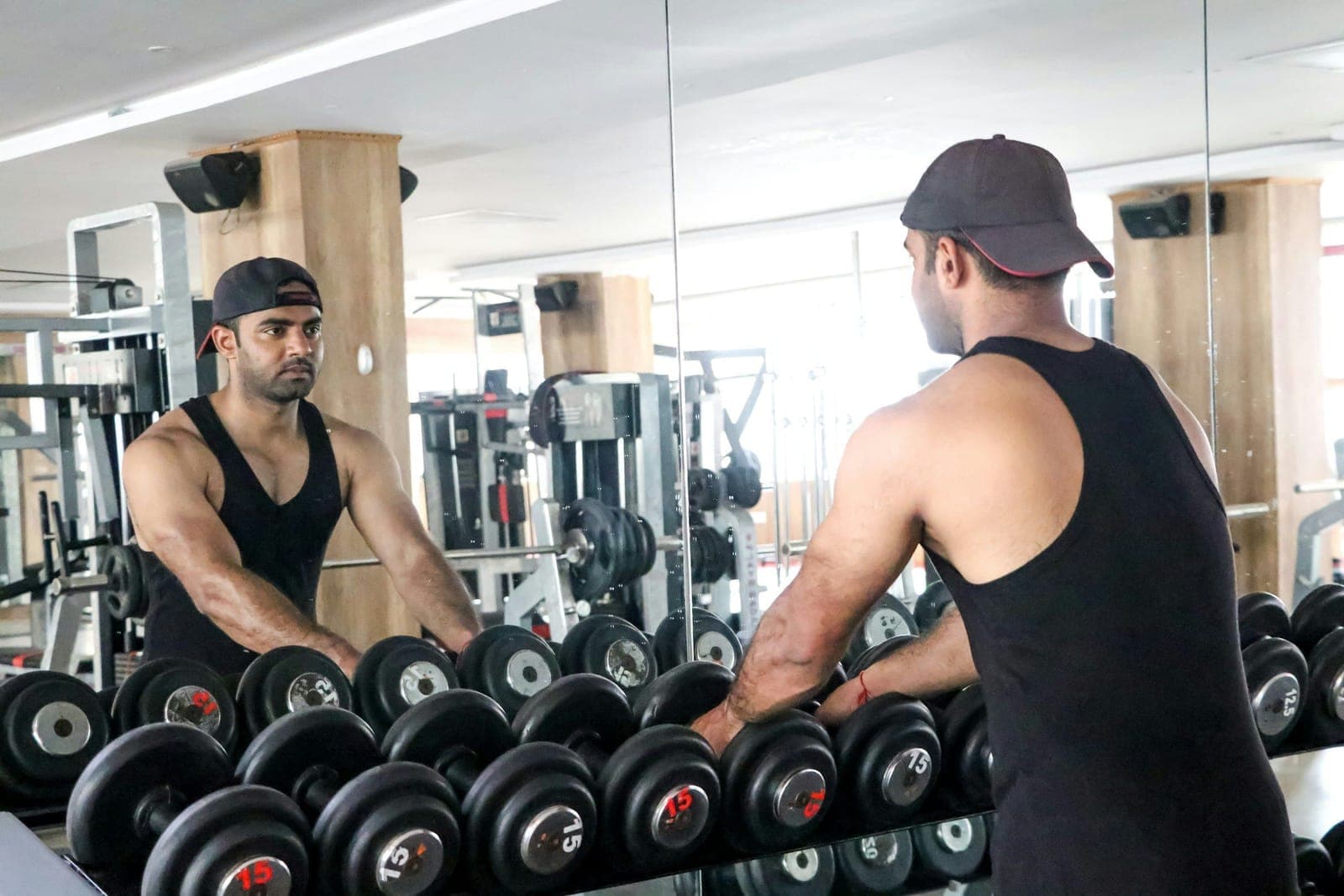 A member at the dumbbell rack, facing the gym mirror